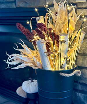 photo of floral arrangement with corn husks, birch wood & lights